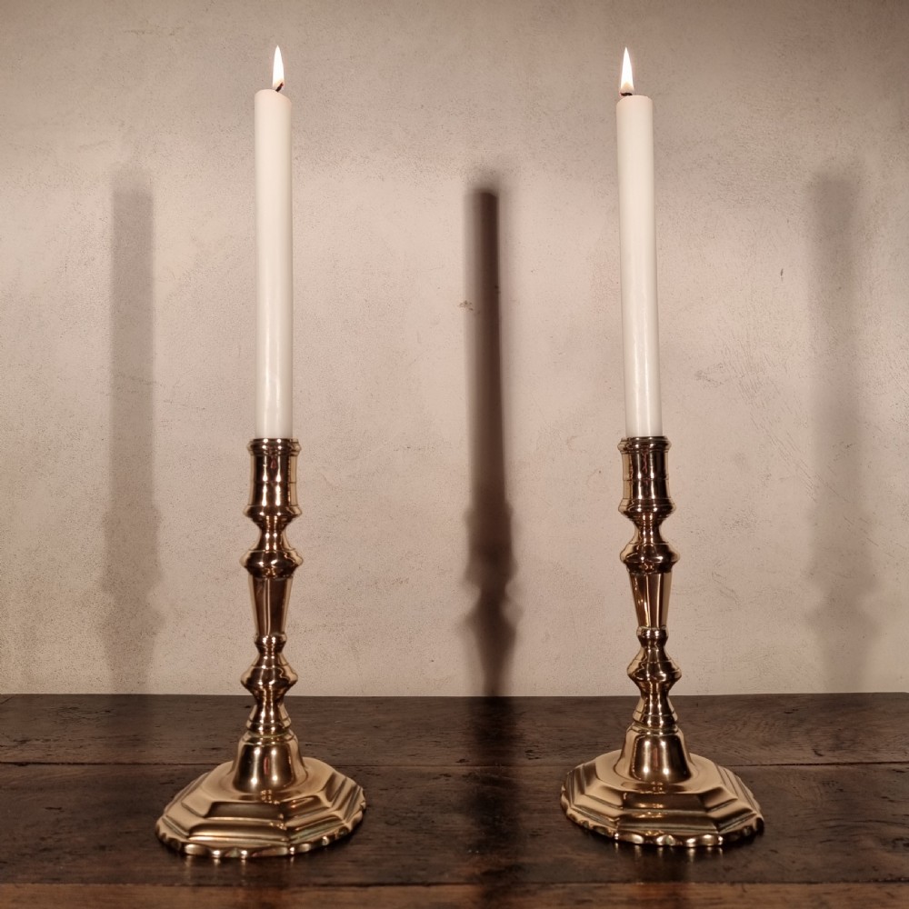 A pair of mid-18th-century cast brass candlesticks featuring knopped stems and octagonal stepped bases holding lit white taper candles. View V