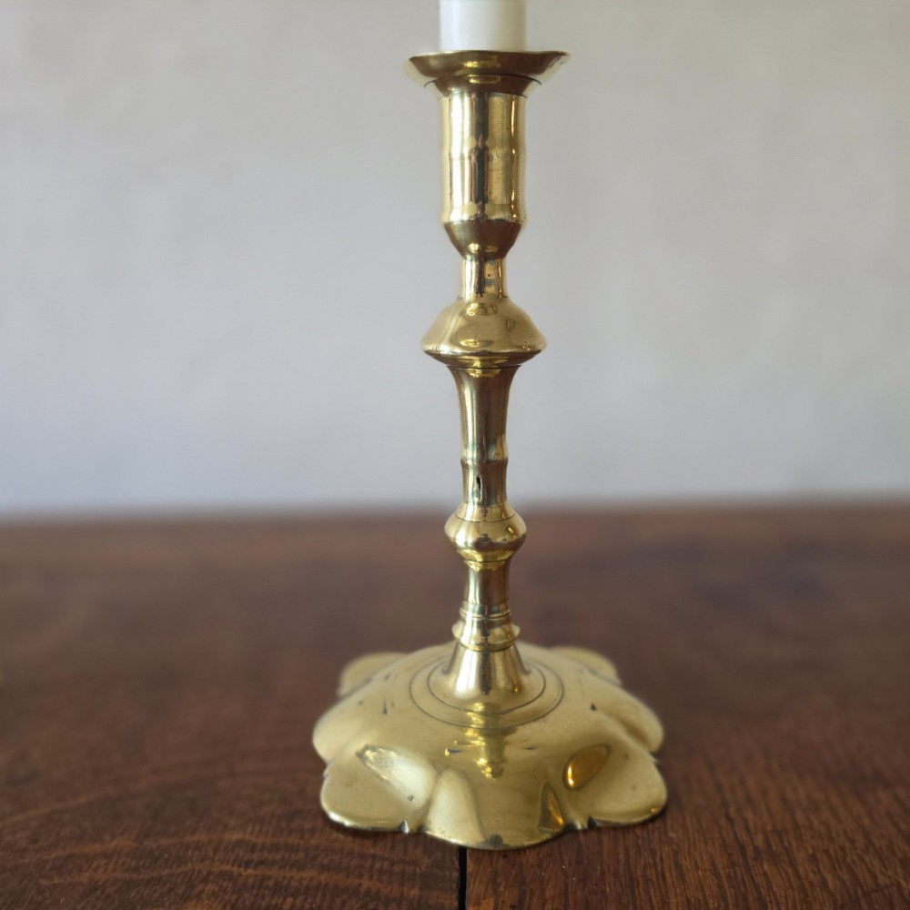 A pair of 18th-century brass candlesticks featuring turned baluster stems and scalloped petal bases, holding lit white taper candles. View III