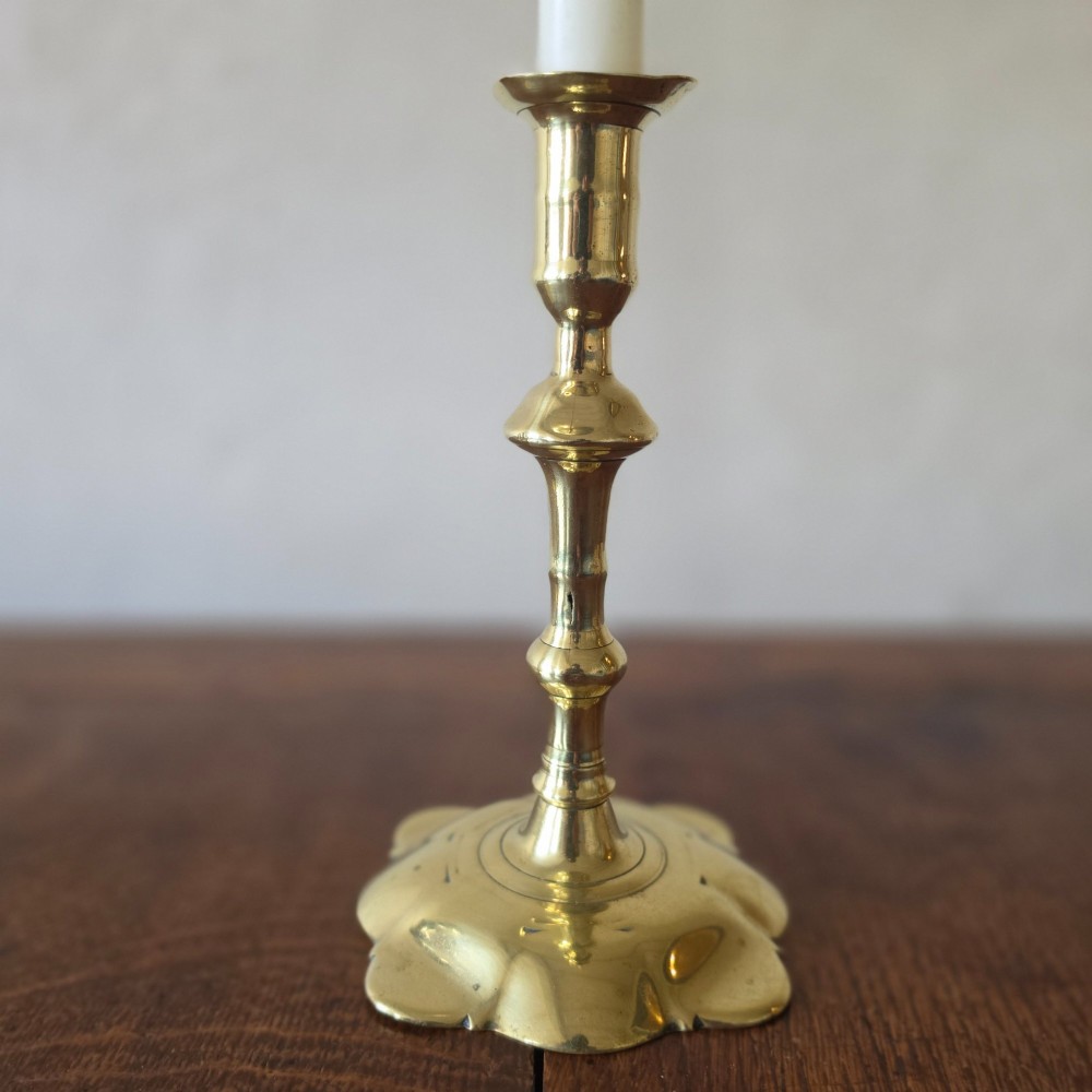 A pair of 18th-century brass candlesticks featuring turned baluster stems and scalloped petal bases, holding lit white taper candles. View IV