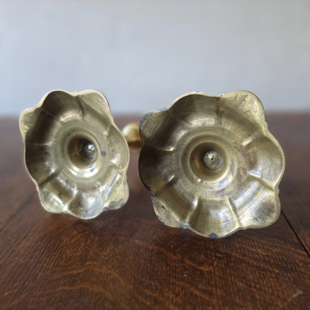 A pair of 18th-century brass candlesticks featuring turned baluster stems and scalloped petal bases, holding lit white taper candles. View VII