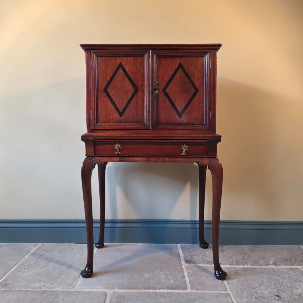 An 18th-century dark wood cabinet on stand featuring twin doors with black diamond inlay, a single lower drawer, and slender cabriole legs.