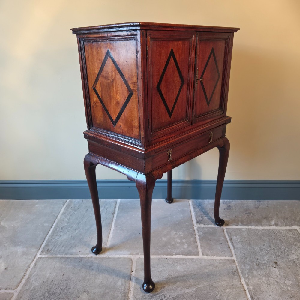 An 18th-century dark wood cabinet on stand featuring twin doors with black diamond inlay, a single lower drawer, and slender cabriole legs. View IX