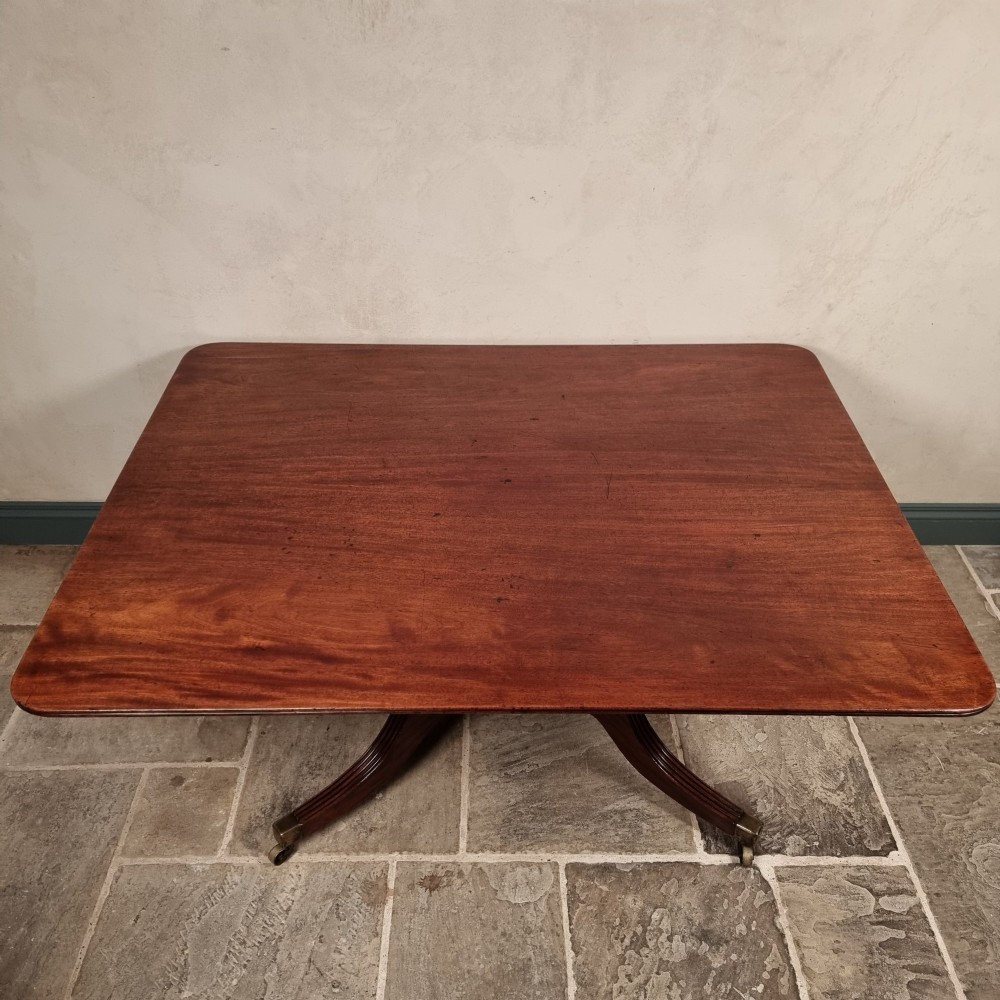 A Regency mahogany tilt-top dining table shown secured vertically on a central pedestal with reeded swept legs and brass castors. View II