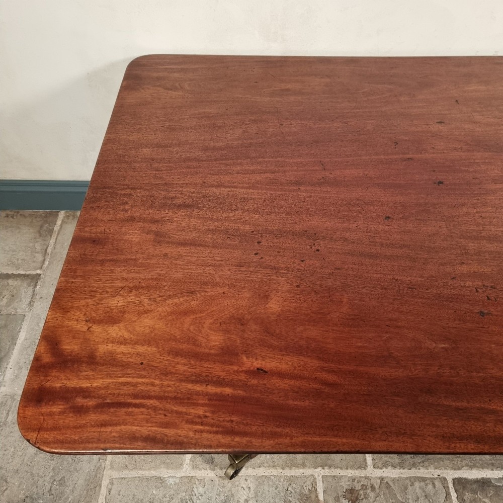 A Regency mahogany tilt-top dining table shown secured vertically on a central pedestal with reeded swept legs and brass castors. View III
