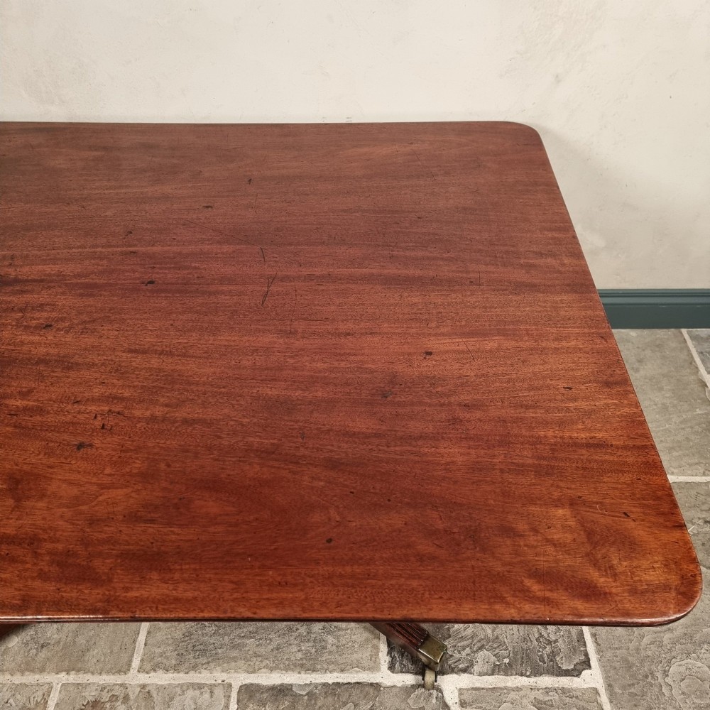 A Regency mahogany tilt-top dining table shown secured vertically on a central pedestal with reeded swept legs and brass castors. View IV