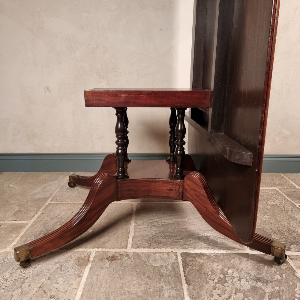 A Regency mahogany tilt-top dining table shown secured vertically on a central pedestal with reeded swept legs and brass castors. View V