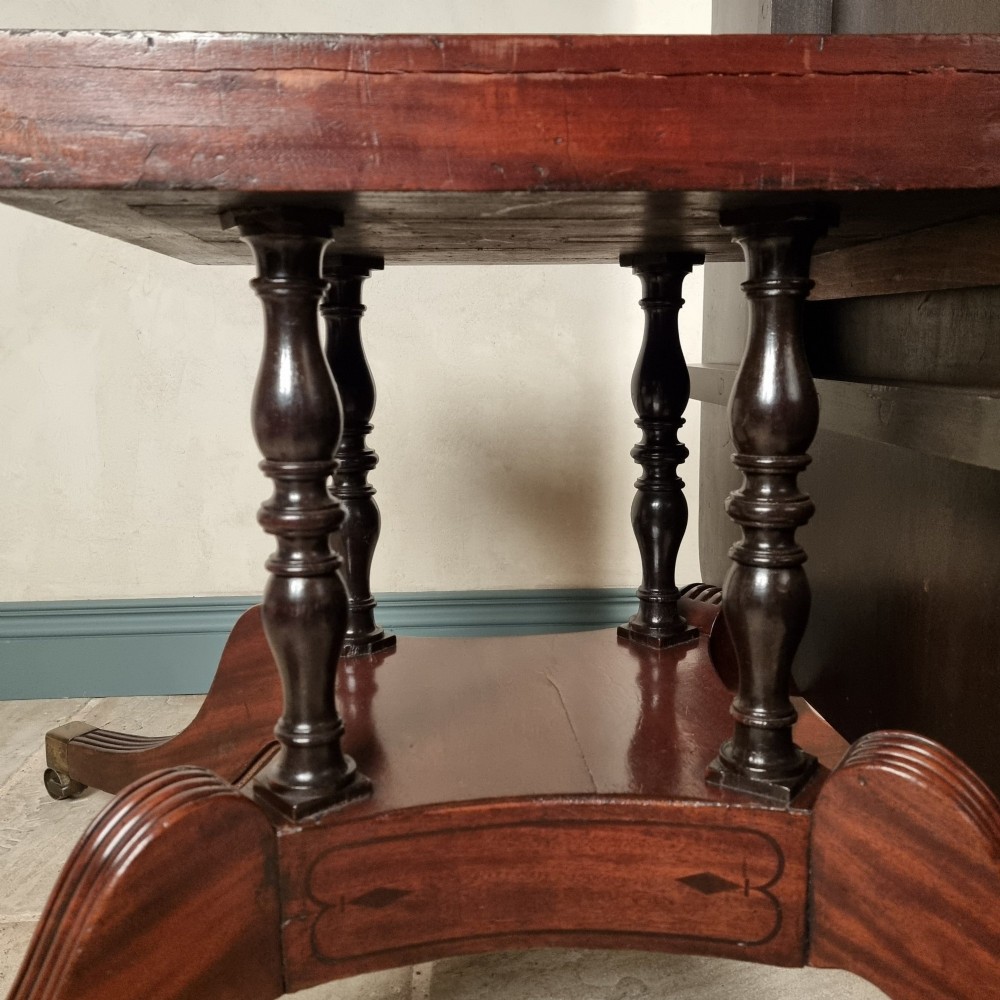 A Regency mahogany tilt-top dining table shown secured vertically on a central pedestal with reeded swept legs and brass castors. View VI
