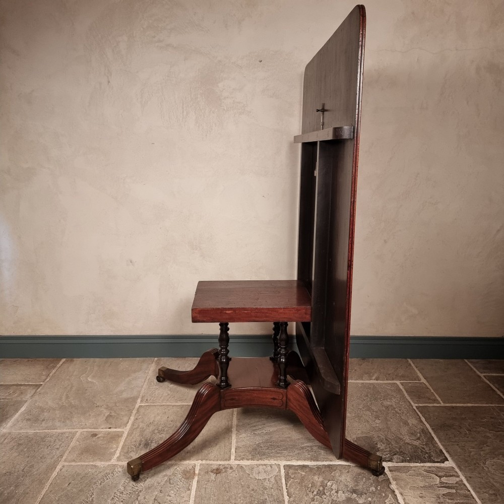 A Regency mahogany tilt-top dining table shown secured vertically on a central pedestal with reeded swept legs and brass castors. View VII