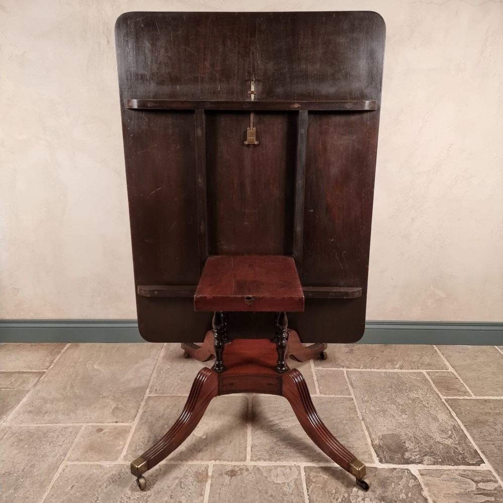 A Regency mahogany tilt-top dining table shown secured vertically on a central pedestal with reeded swept legs and brass castors. View IX