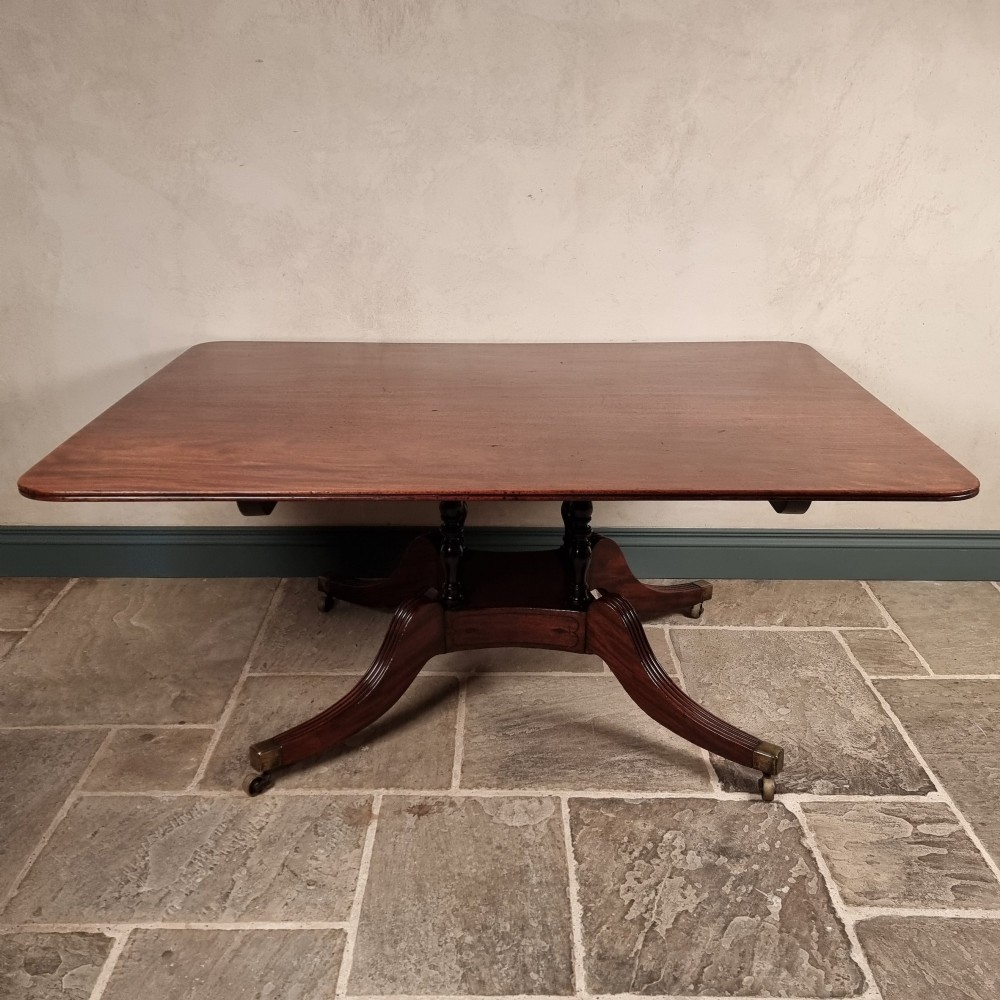A Regency mahogany tilt-top dining table shown secured vertically on a central pedestal with reeded swept legs and brass castors. View X