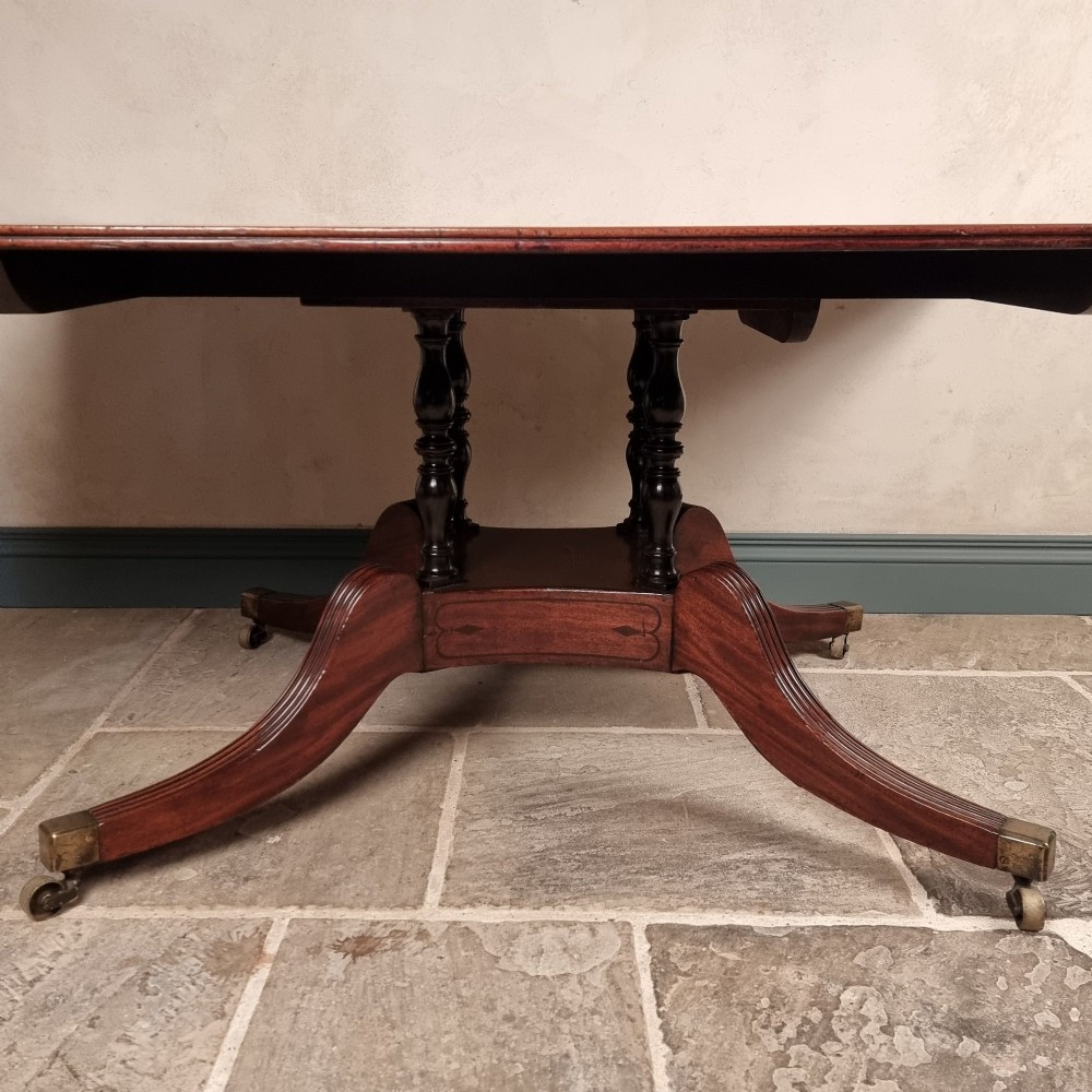 A Regency mahogany tilt-top dining table shown secured vertically on a central pedestal with reeded swept legs and brass castors. View XI