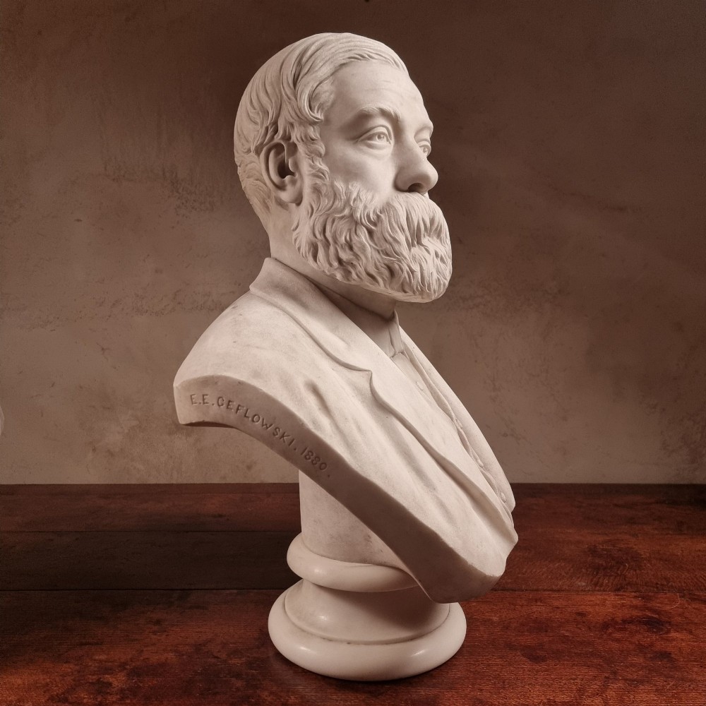A pair of carved white marble portrait busts depicting a classical female figure on the left and a bearded man in Victorian attire on the right. View IV