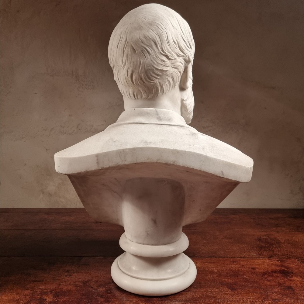A pair of carved white marble portrait busts depicting a classical female figure on the left and a bearded man in Victorian attire on the right. View V