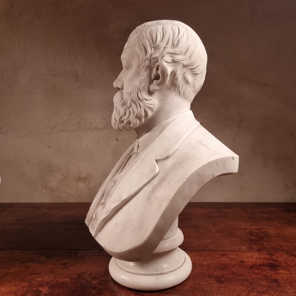 A pair of carved white marble portrait busts depicting a classical female figure on the left and a bearded man in Victorian attire on the right. View VI