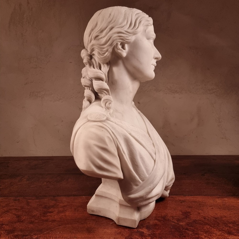 A pair of carved white marble portrait busts depicting a classical female figure on the left and a bearded man in Victorian attire on the right. View IX