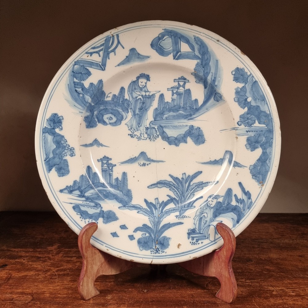 A circular 17th century tin-glazed earthenware Delft charger hand-painted with cobalt blue Chinoiserie figures and foliage against a creamy white ground.