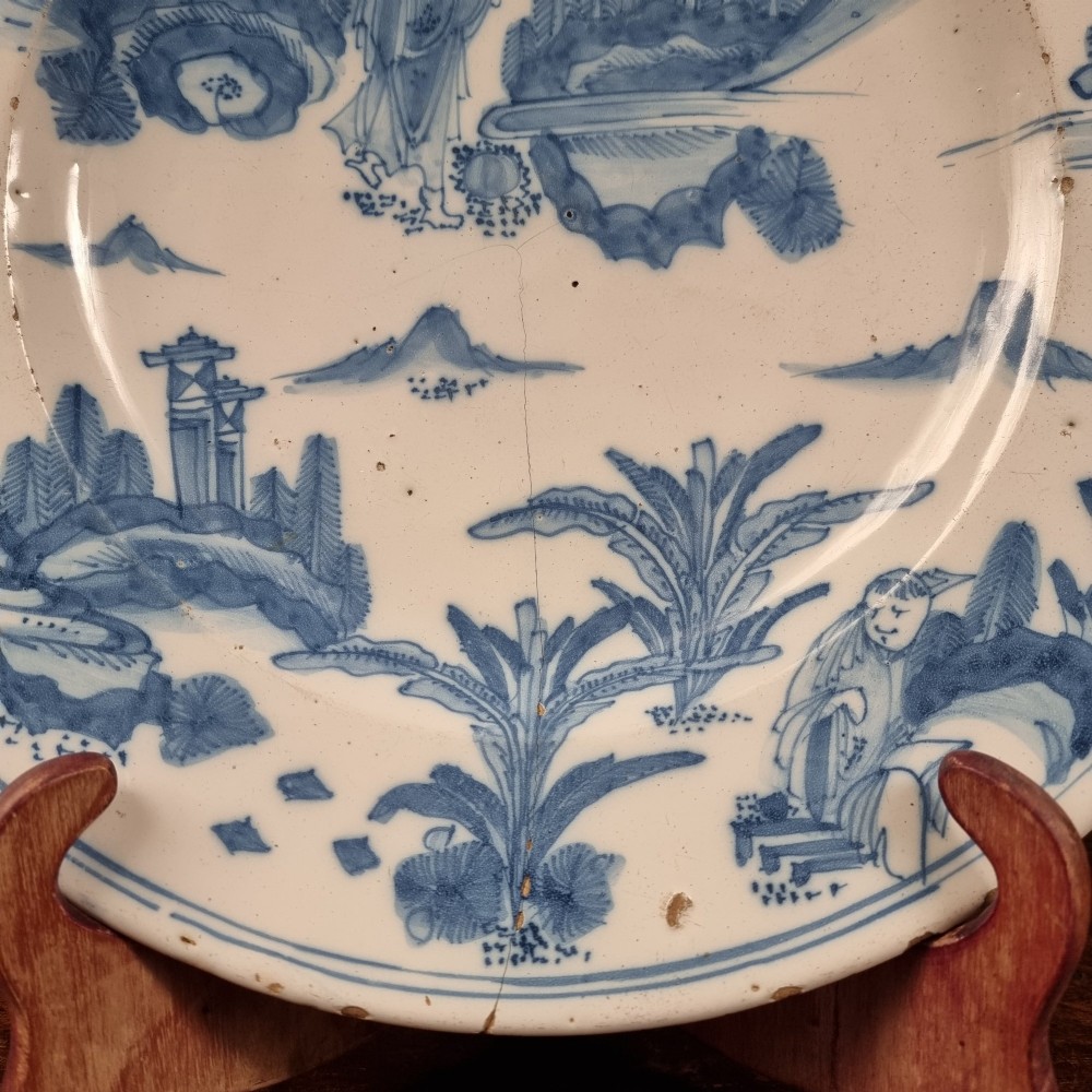 A circular 17th century tin-glazed earthenware Delft charger hand-painted with cobalt blue Chinoiserie figures and foliage against a creamy white ground. View II