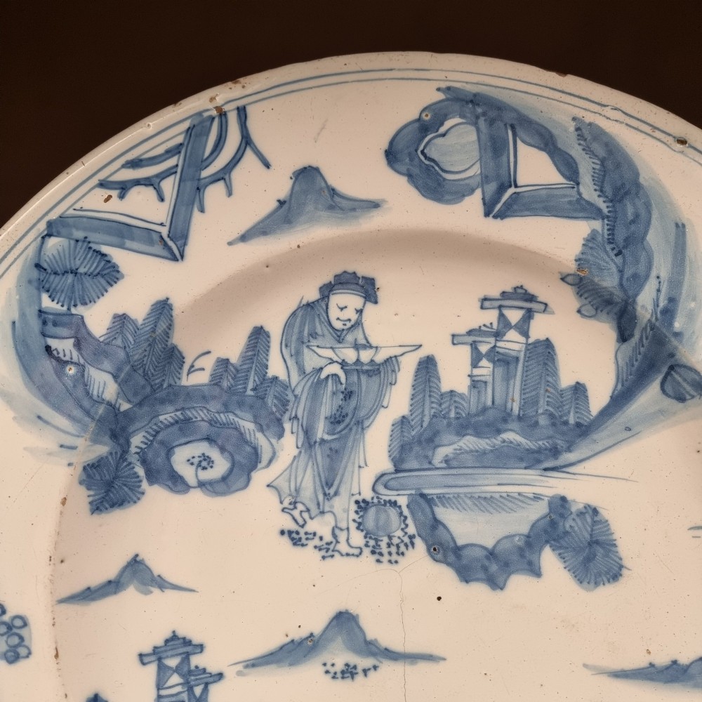 A circular 17th century tin-glazed earthenware Delft charger hand-painted with cobalt blue Chinoiserie figures and foliage against a creamy white ground. View III