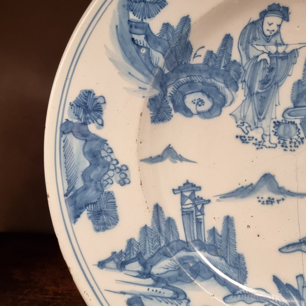 A circular 17th century tin-glazed earthenware Delft charger hand-painted with cobalt blue Chinoiserie figures and foliage against a creamy white ground. View IV