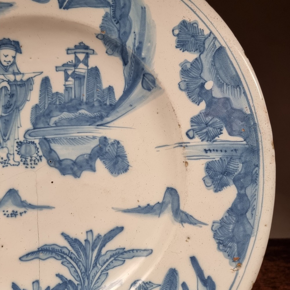 A circular 17th century tin-glazed earthenware Delft charger hand-painted with cobalt blue Chinoiserie figures and foliage against a creamy white ground. View V
