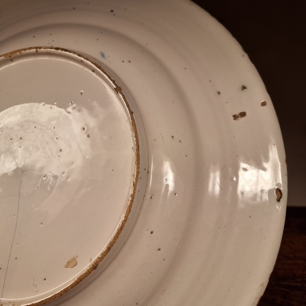 A circular 17th century tin-glazed earthenware Delft charger hand-painted with cobalt blue Chinoiserie figures and foliage against a creamy white ground. View X