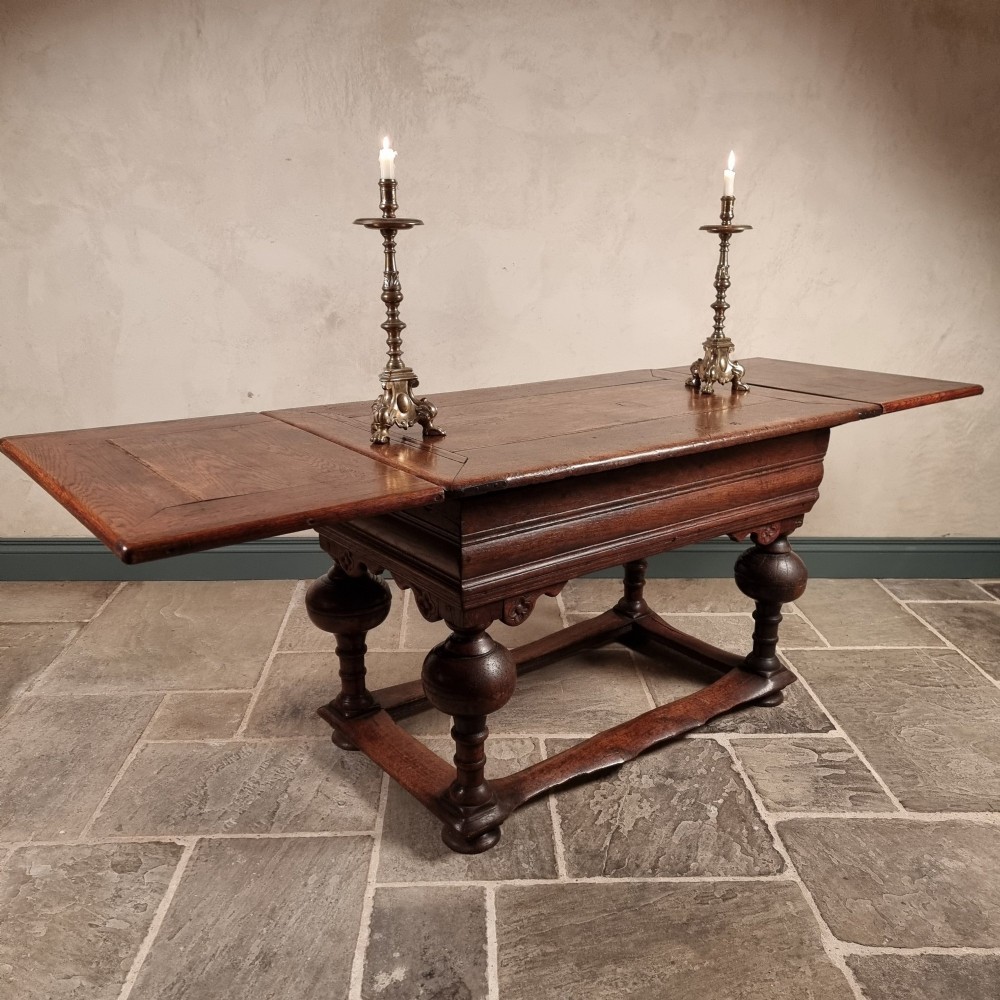 A dark oak seventeenth-century refectory dining table with extensible draw leaves, bulbous turned legs, and a floor-level perimeter stretcher.