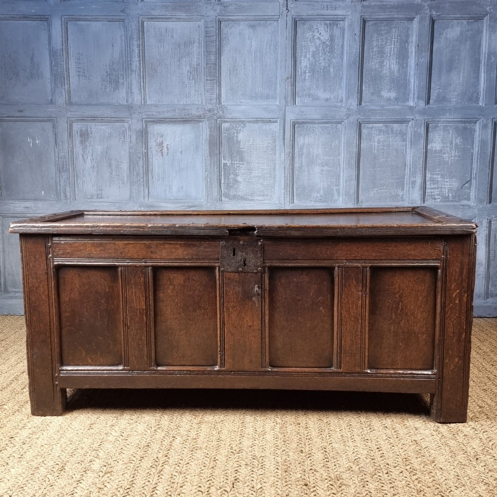 A late Elizabethan dark oak coffer with a rectangular hinged lid, iron lockplate, and panelled front facade.