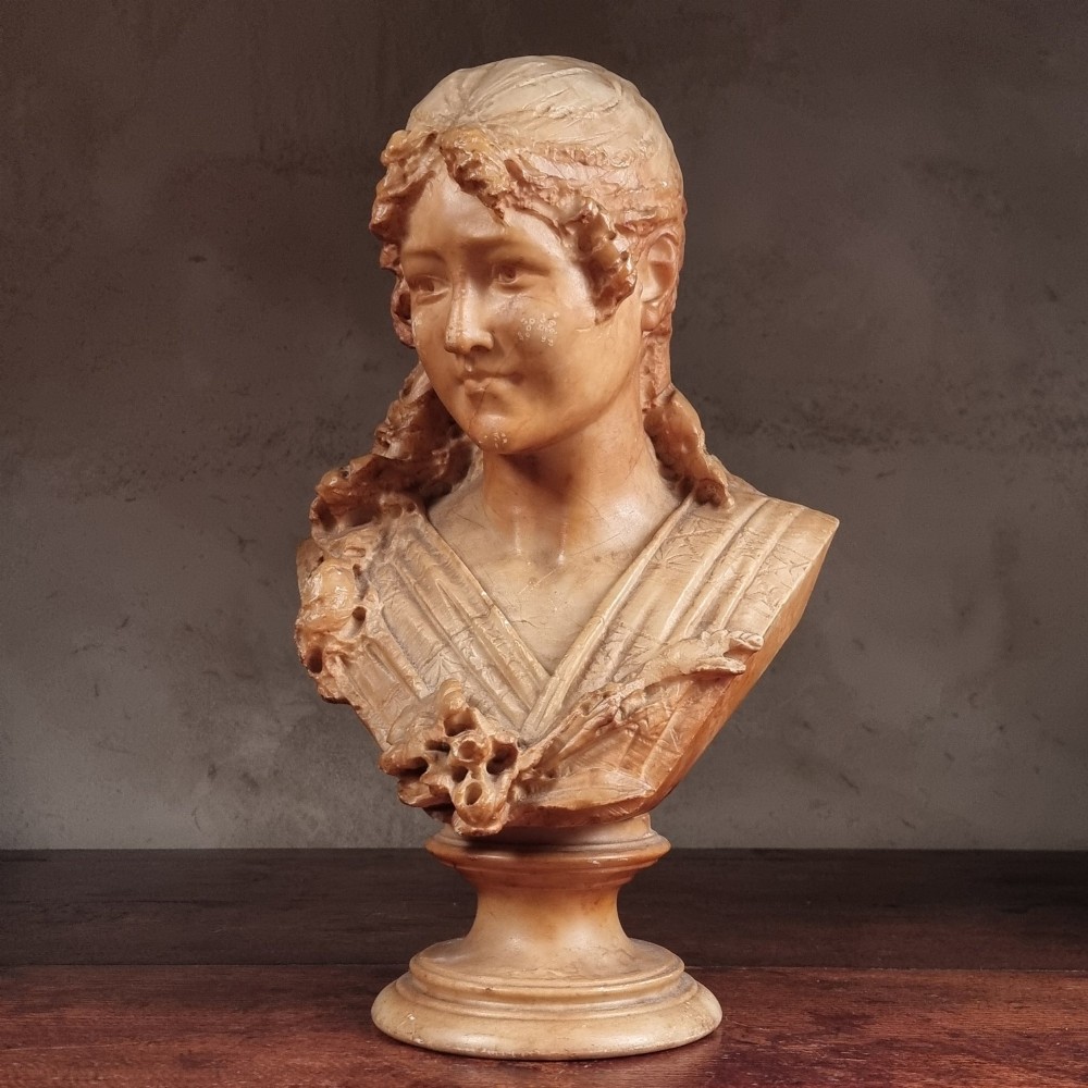 A 19th-century carved alabaster bust depicting a young woman with wavy hair and draped clothing mounted on a turned pedestal base.