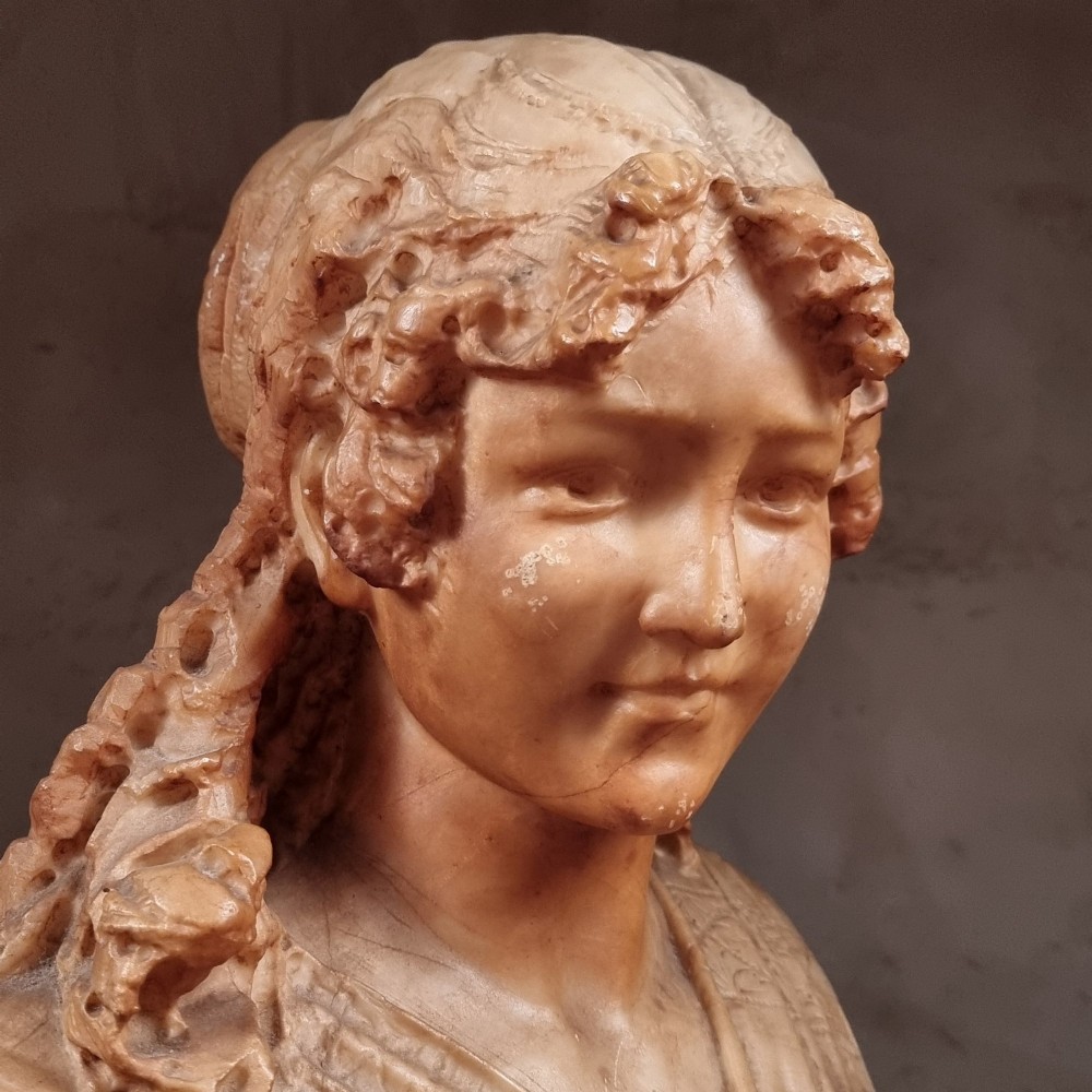 A 19th-century carved alabaster bust depicting a young woman with wavy hair and draped clothing mounted on a turned pedestal base. View II