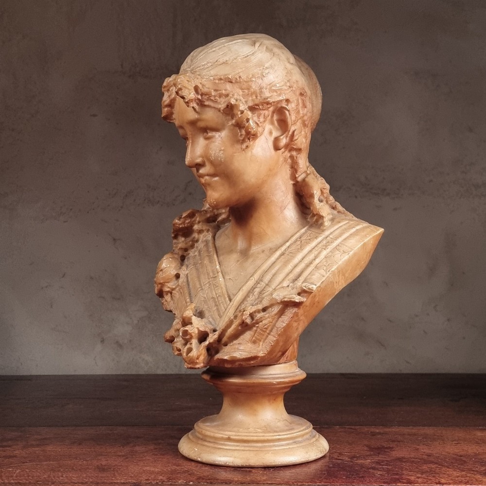 A 19th-century carved alabaster bust depicting a young woman with wavy hair and draped clothing mounted on a turned pedestal base. View IV