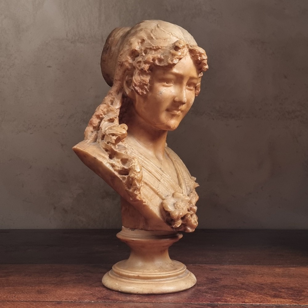 A 19th-century carved alabaster bust depicting a young woman with wavy hair and draped clothing mounted on a turned pedestal base. View V