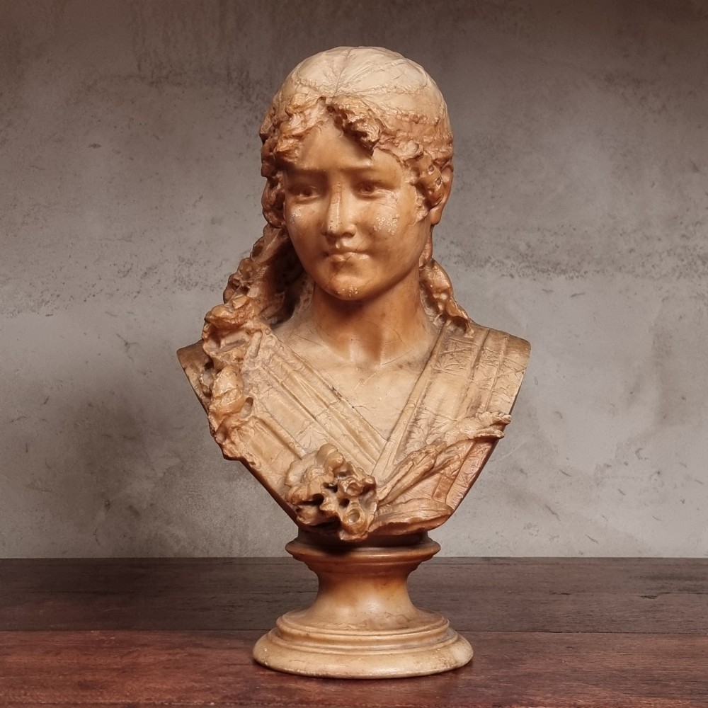 A 19th-century carved alabaster bust depicting a young woman with wavy hair and draped clothing mounted on a turned pedestal base. View VI