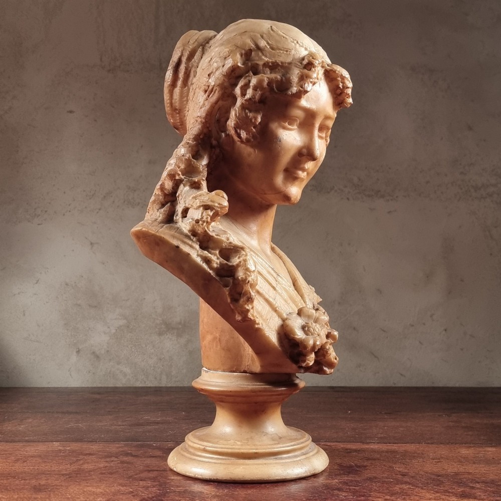 A 19th-century carved alabaster bust depicting a young woman with wavy hair and draped clothing mounted on a turned pedestal base. View VIII