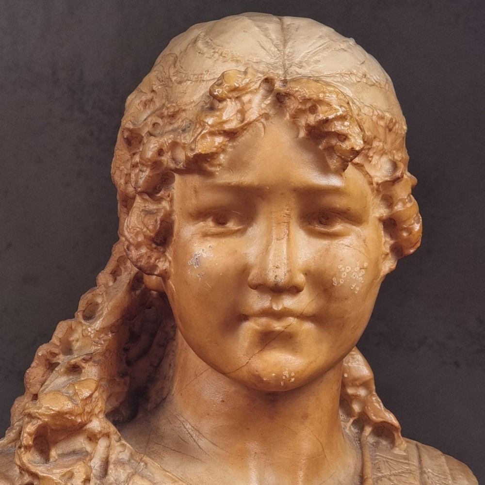 A 19th-century carved alabaster bust depicting a young woman with wavy hair and draped clothing mounted on a turned pedestal base. View IX