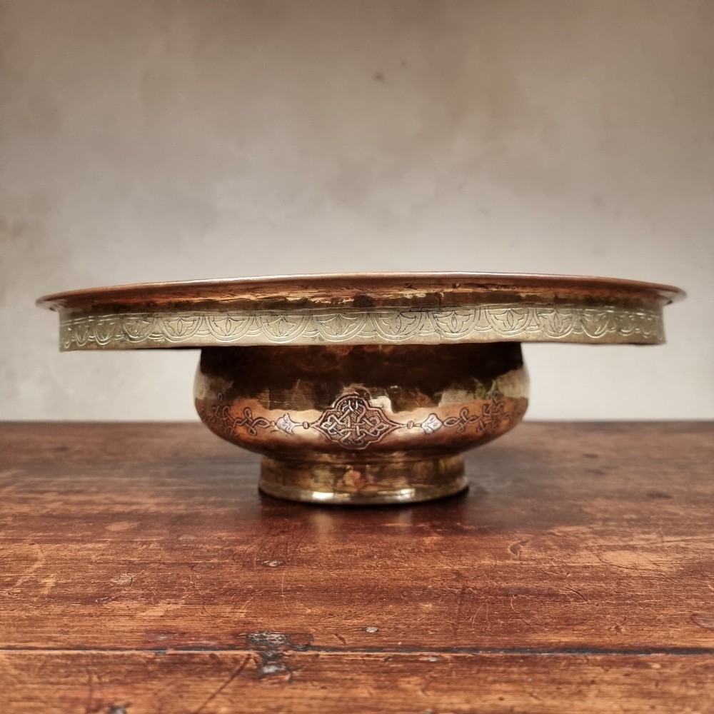 A circular 19th-century Islamic brass wash bowl featuring intricate Arabic calligraphic script, geometric arabesque patterns, pierced metalwork, and silver and copper inlay. View VII