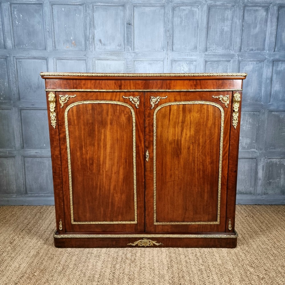 A 19th-century flame mahogany enclosed chest featuring twin doors framed with gilded metal moulding and corner mounts.
