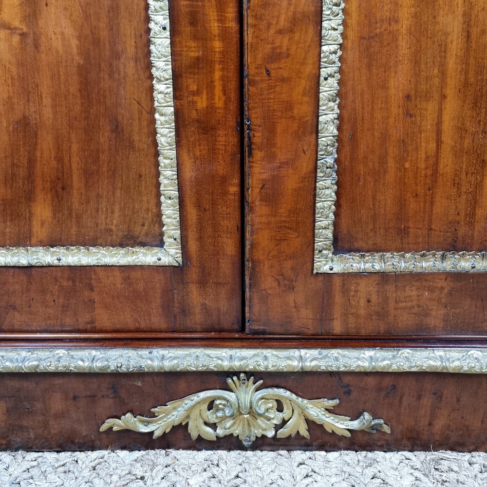 A 19th-century flame mahogany enclosed chest featuring twin doors framed with gilded metal moulding and corner mounts. View IV