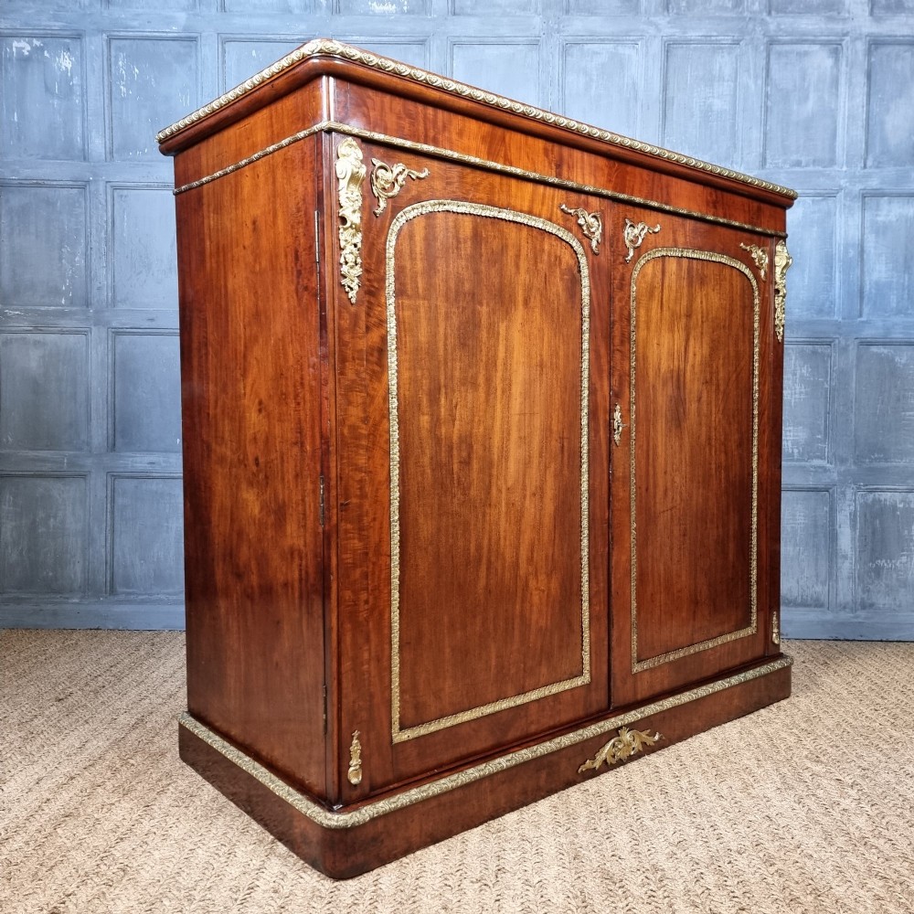 A 19th-century flame mahogany enclosed chest featuring twin doors framed with gilded metal moulding and corner mounts. View X
