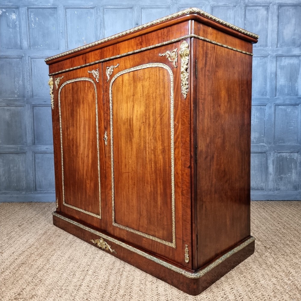 A 19th-century flame mahogany enclosed chest featuring twin doors framed with gilded metal moulding and corner mounts. View XI