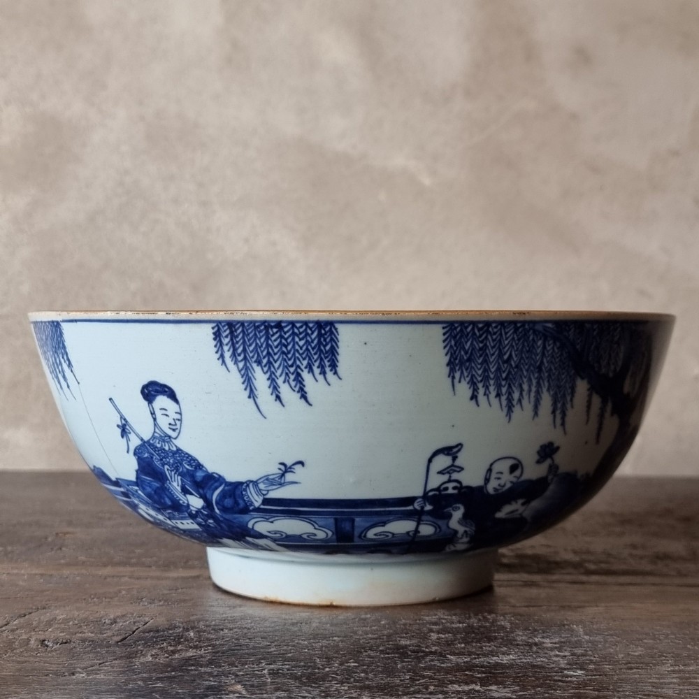 An 18th-century circular Chinese export porcelain punch bowl decorated with hand-painted blue figures under a willow tree.