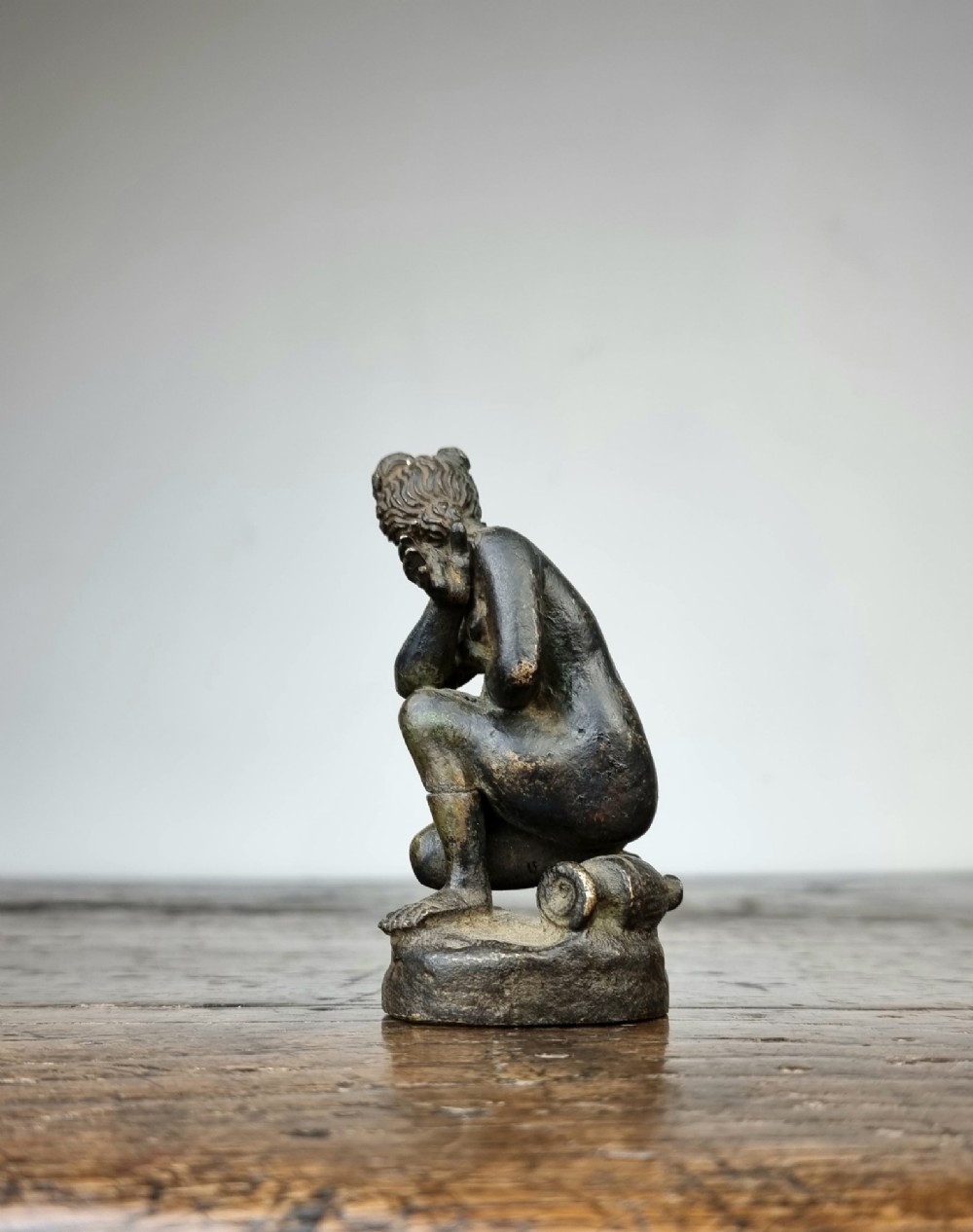 A small 17th-century dark bronze statuette depicting the mythological figure Crouching Venus seated on an integral rock base. View V