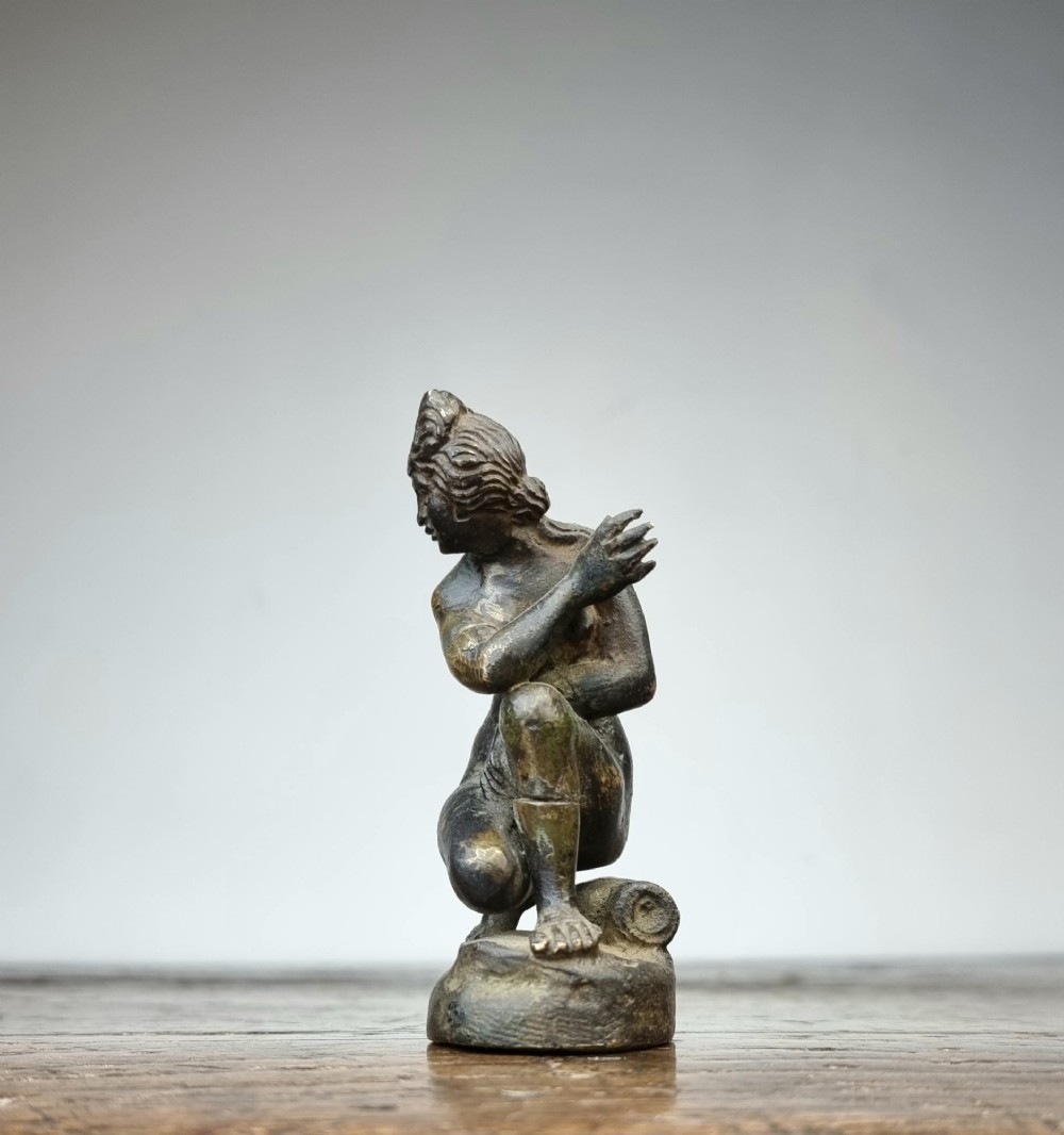 A small 17th-century dark bronze statuette depicting the mythological figure Crouching Venus seated on an integral rock base. View VI