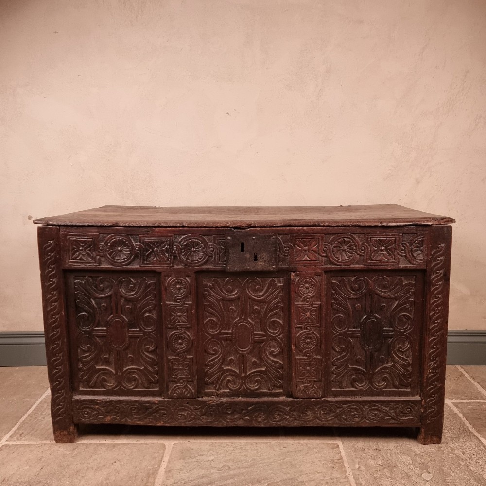 A dark carved oak early 17th-century coffer featuring decorated scrollwork panels and a central iron lockplate.