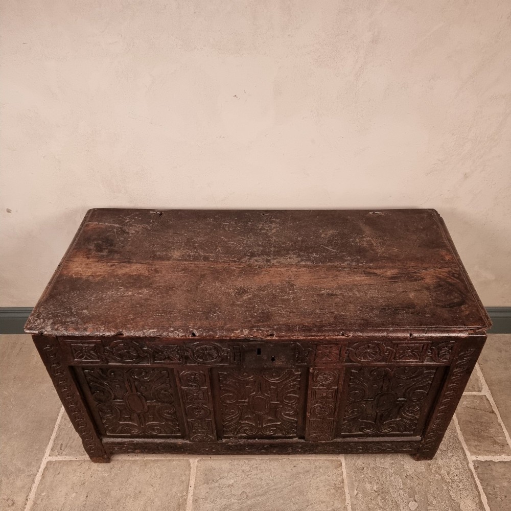 A dark carved oak early 17th-century coffer featuring decorated scrollwork panels and a central iron lockplate. View II