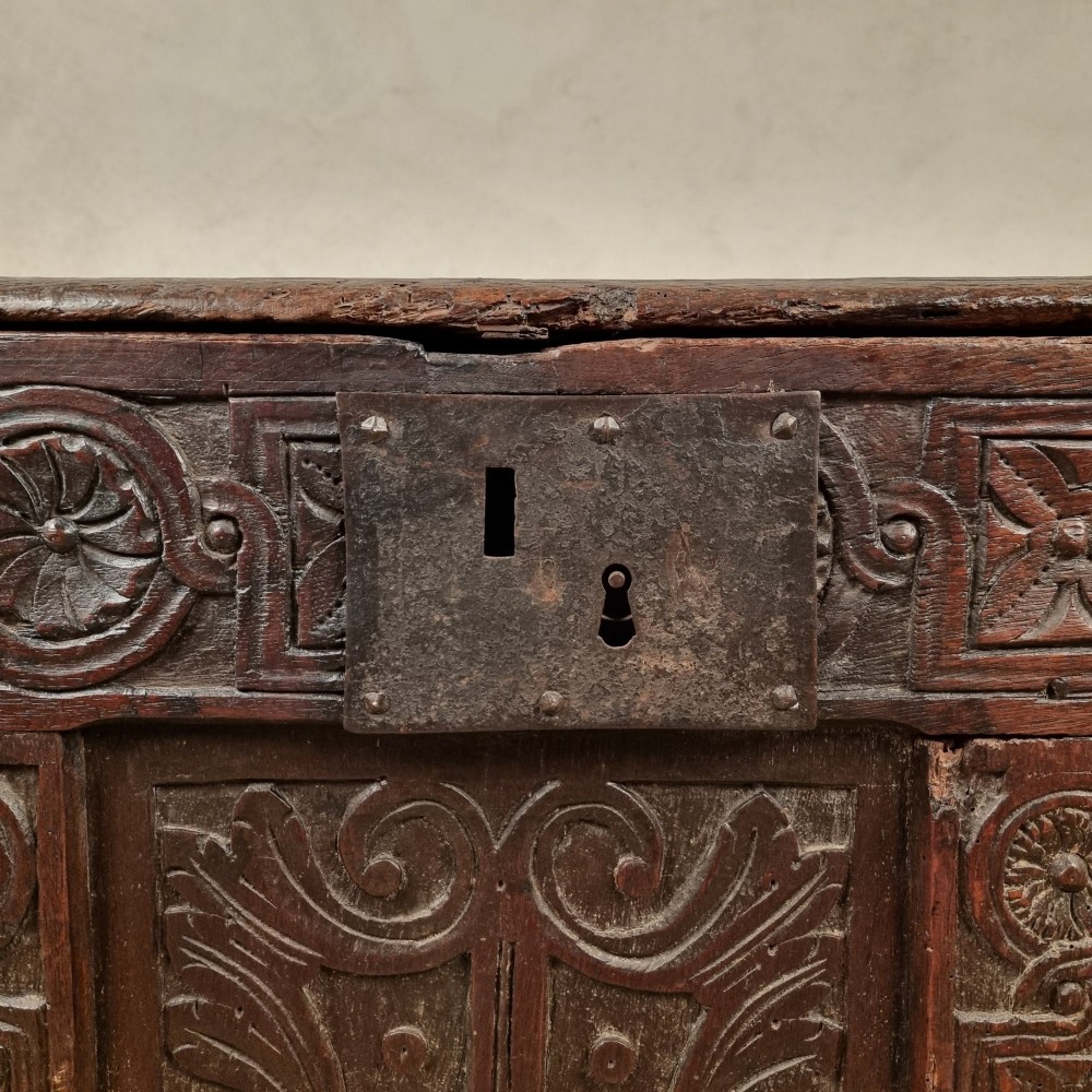 A dark carved oak early 17th-century coffer featuring decorated scrollwork panels and a central iron lockplate. View VII
