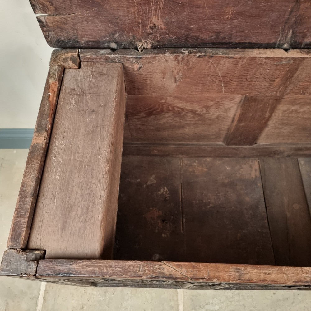A dark carved oak early 17th-century coffer featuring decorated scrollwork panels and a central iron lockplate. View X
