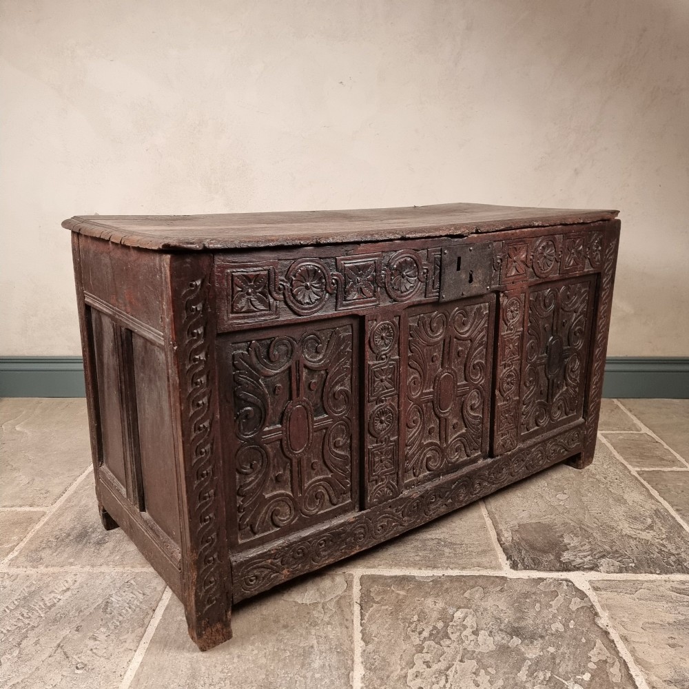 A dark carved oak early 17th-century coffer featuring decorated scrollwork panels and a central iron lockplate. View XI