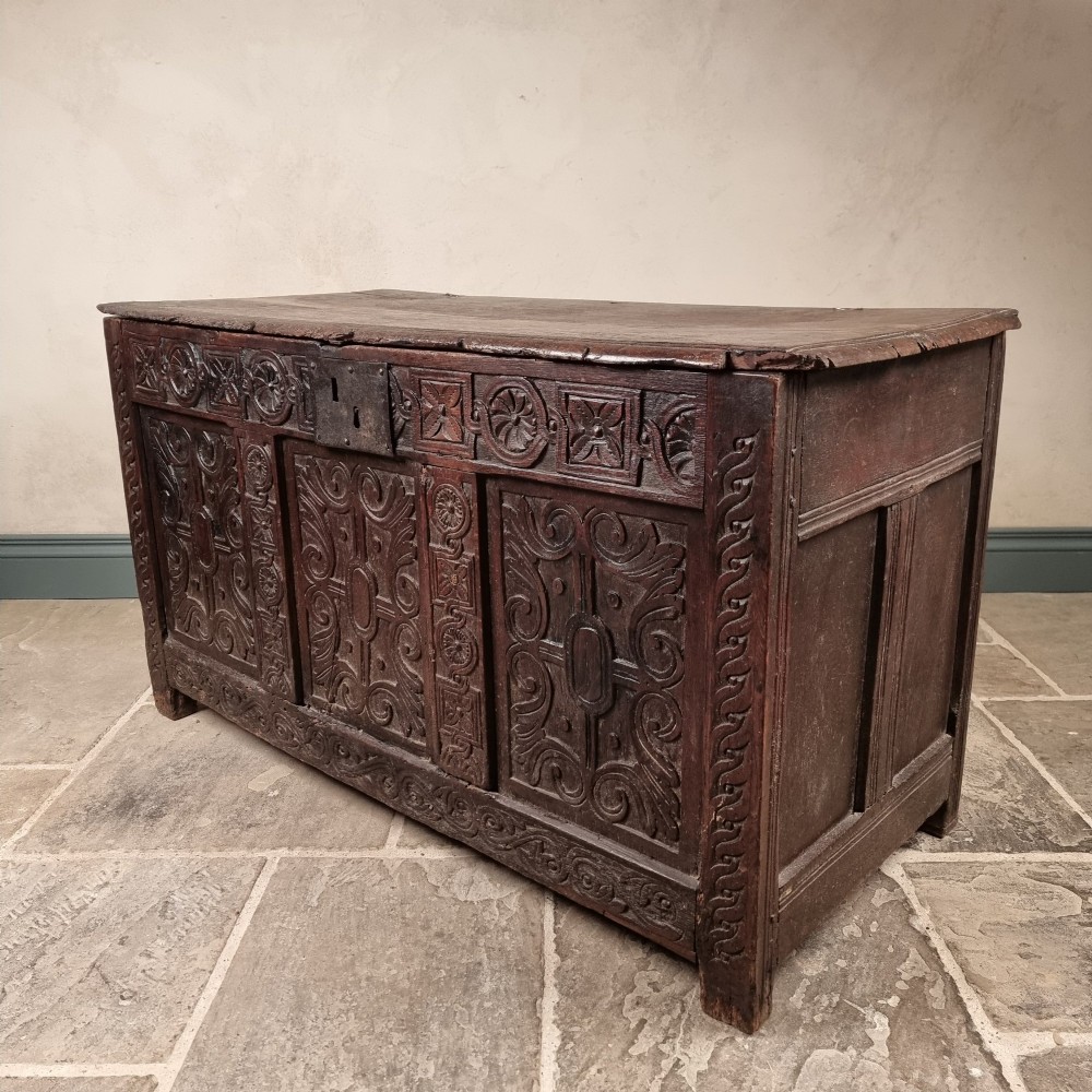 A dark carved oak early 17th-century coffer featuring decorated scrollwork panels and a central iron lockplate. View XII