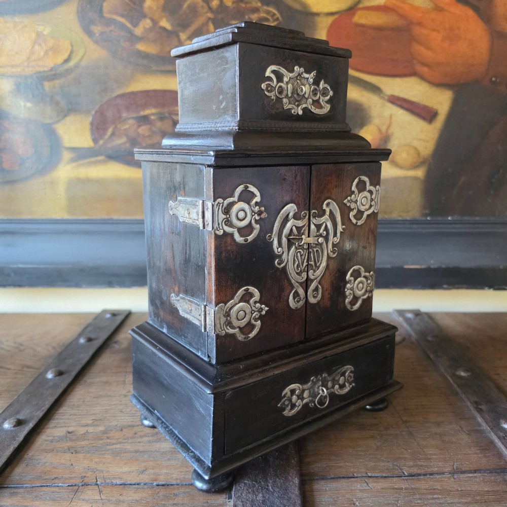 A tiered 18th-century walnut jewellery cabinet featuring ornate silvered metal hinges, a central latch mechanism, a lower drawer, and turned bun feet. View II