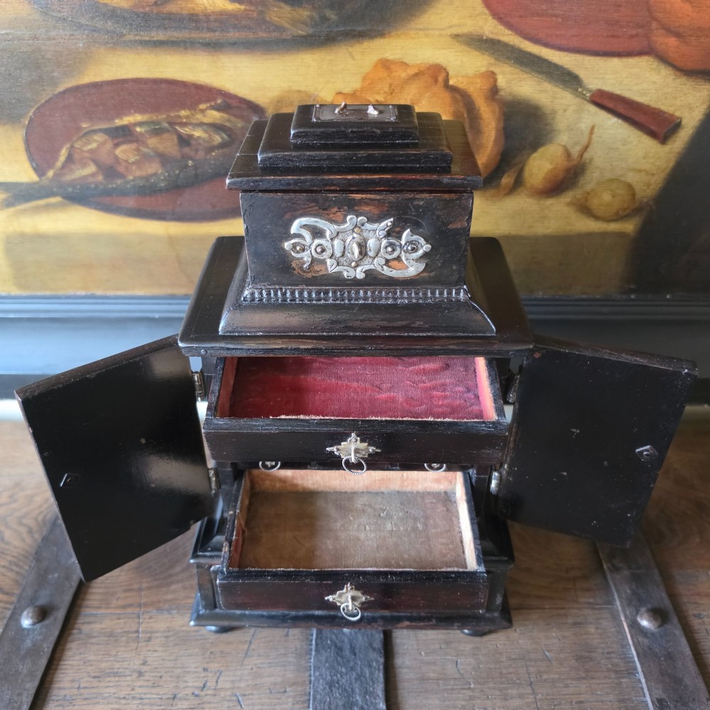 A tiered 18th-century walnut jewellery cabinet featuring ornate silvered metal hinges, a central latch mechanism, a lower drawer, and turned bun feet. View VII